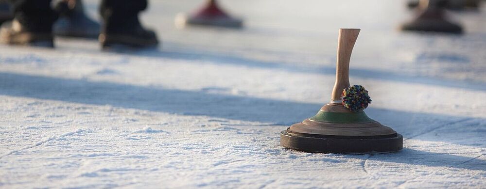 Der ta Expi-Cup findet in Mörlenbach statt Personen stehen auf einer vereisten Fläche und spielen Eisstockschießen; mehrere Eisstöcke liegen auf dem Eis, einer im Vordergrund ist scharf zu sehen.