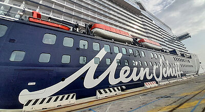 Auch Adults-only-Kreuzfahrten mit der Mein Schiff Relax finden sich im neuen Programm von TUI Cruises. Foto: ck Seitenansicht eines großen Kreuzfahrtschiffes an der Pier. Auf dem dunkelblauen Rumpf prangt groß in Schreibschrift der Name Mein Schiff.